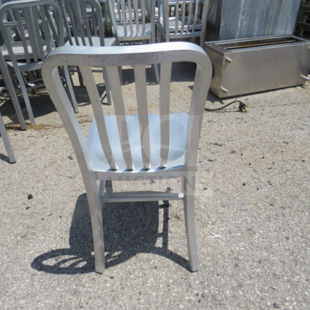 Silver aluminum chair, suitable for indoor/outdoor use. Features slatted back design, shown in used condition.