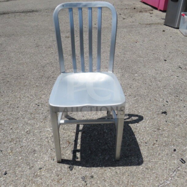 Silver aluminum indoor/outdoor chair, featuring a slatted backrest and contoured seat. Durable, weather-resistant finish.
