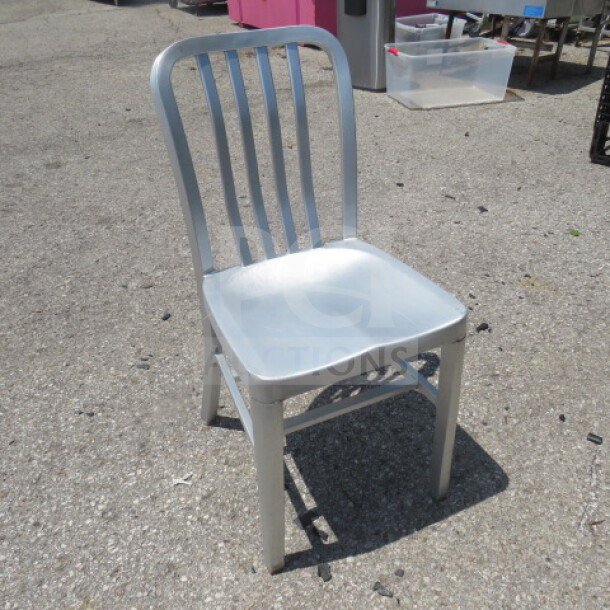 Silver aluminum indoor/outdoor chair, slatted back, durable construction, suitable for versatile use. Light wear visible.