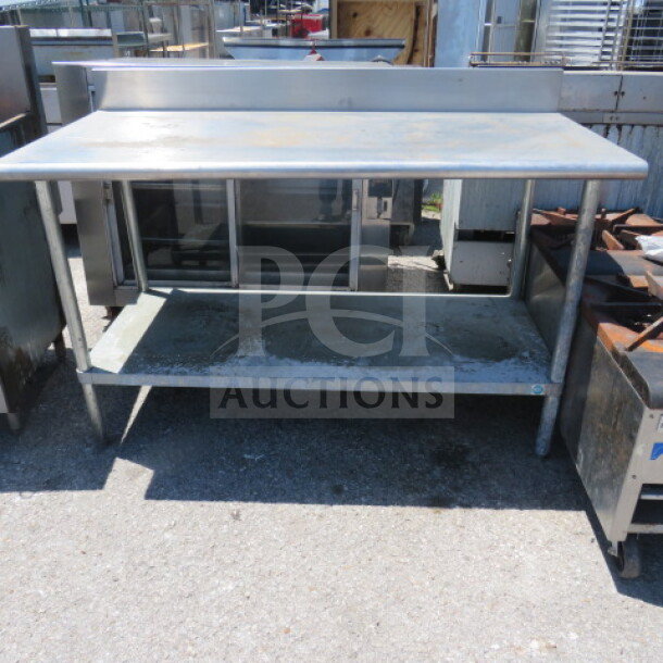Stainless steel table with under shelf, used, showing slight wear. Ideal for kitchen or industrial use.
