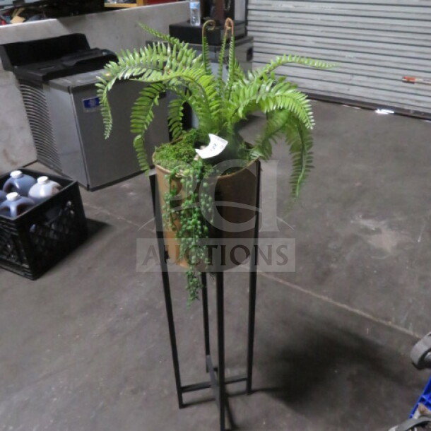 Potted fern in a metal stand, featuring cascading greenery. Good condition. Indoor setting, identifiable item tag present.