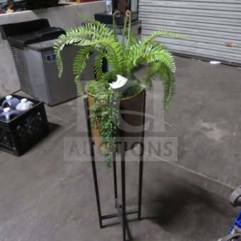 Potted fern in a metal stand, featuring cascading greenery. Good condition. Indoor setting, identifiable item tag present.