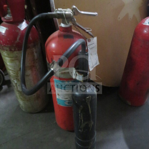 Red fire extinguisher with attached hose and nozzle, visible wear, label with usage instructions.