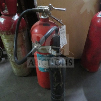 Red fire extinguisher with attached hose and nozzle, visible wear, label with usage instructions.