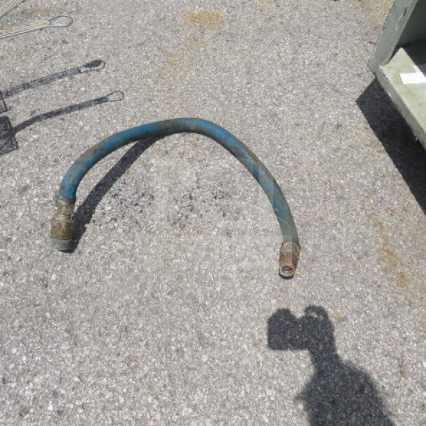 Vintage gas hose, blue, with connectors on both ends, in used condition on gravel surface. Suitable for specific machinery.