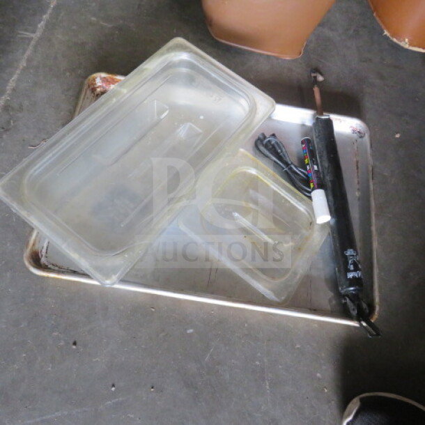 One lot of miscellaneous items including plastic trays, a metal tray, and a black tool with attached wires on a concrete floor.
