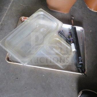 One lot of miscellaneous items including plastic trays, a metal tray, and a black tool with attached wires on a concrete floor.
