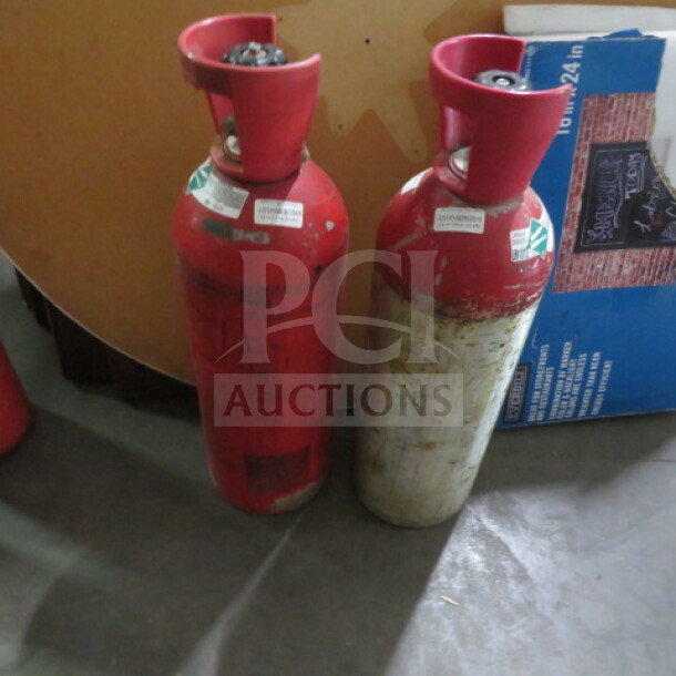 Two red carbon dioxide canisters with red caps, showing signs of wear. Labels with "2XBID NO SHIPPING" visible.