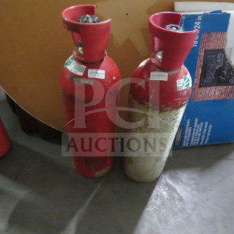 Two red carbon dioxide canisters with red caps, showing signs of wear. Labels with "2XBID NO SHIPPING" visible.