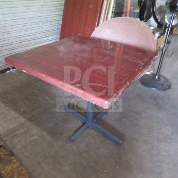 Wooden pedestal table, 36x36x30 inches, square top, noticeable wear, sturdy black base, ideal for dining or office use.