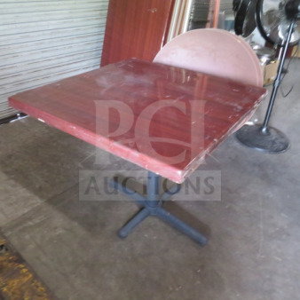 Wooden table with pedestal base, 36x36x30 inches. Shows surface wear, red-finish top, and black metal base. Appears sturdy.