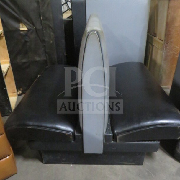Black and gray double-sided cushioned booth in used condition, featuring black seating with a gray divider.
