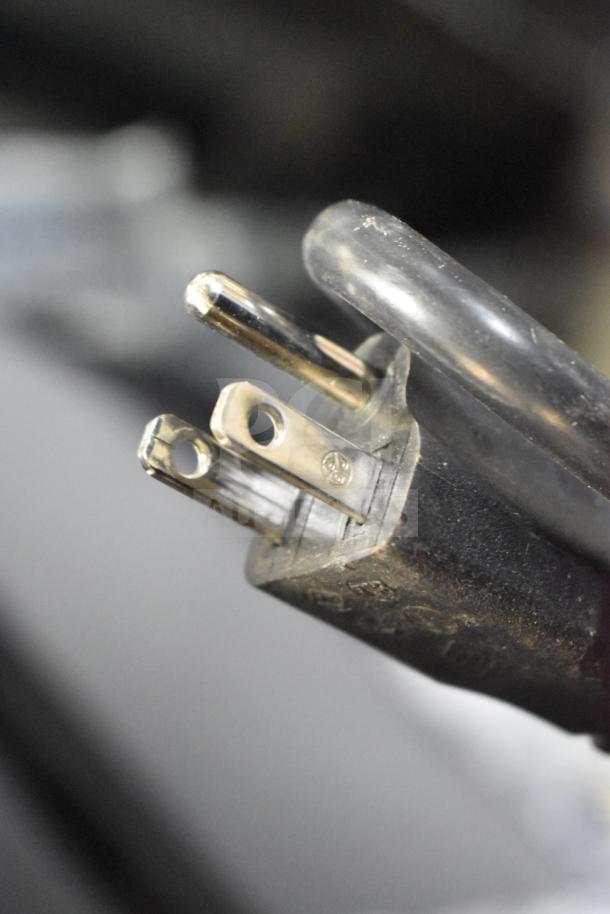 Close-up of the power plug for a Berkel B10-SLC meat slicer, showing three metal prongs and a black casing.