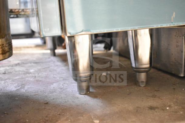 US Range Commercial Counter with stainless steel legs. Item shows signs of wear, ideal for restaurant or industrial use.
