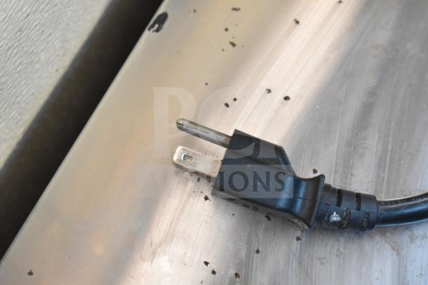 Power cord of Sharp R-21LCFS countertop microwave oven, showing standard two-prong plug, on metallic surface.