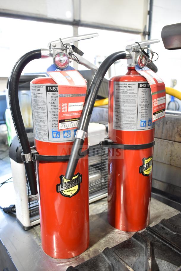 Two red Buckeye fire extinguishers and a bug zapper. Fire extinguishers show operational labels and service dates.