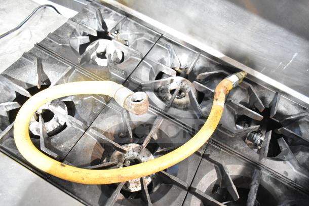 American Range commercial 6 burner stove top with visible gas hose, featuring a sturdy backsplash. Condition shows signs of use.