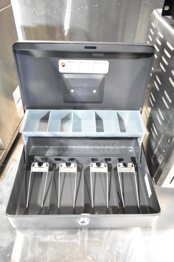 SentrySafe metal cash box with coin compartments and bill clips, open lid, black finish, visible warning label, secure lock.