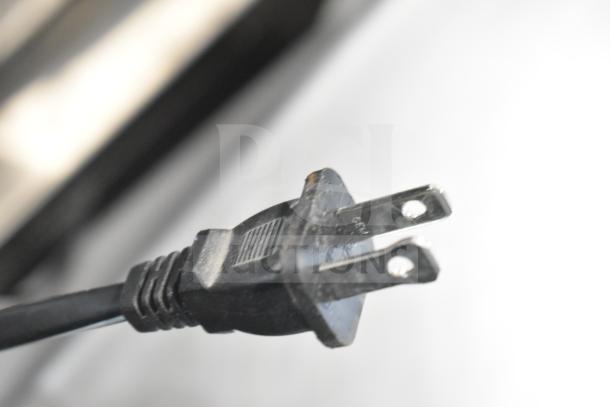 Close-up of a standard two-prong electrical plug with a black cord, likely for an electronic auction item.