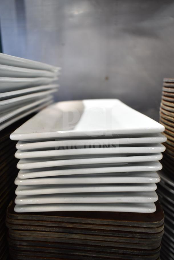 Stack of white rectangular plates, in good condition, displayed on a shelf, part of a mixed lot including baskets.