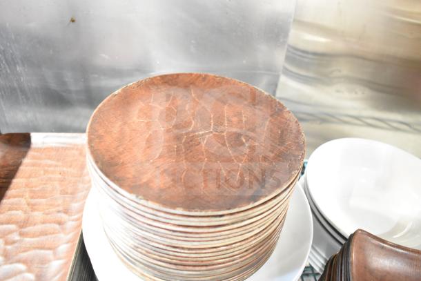 Stack of round wooden plates with a brown, textured surface, mixed with white ceramic plates. Visible signs of wear.
