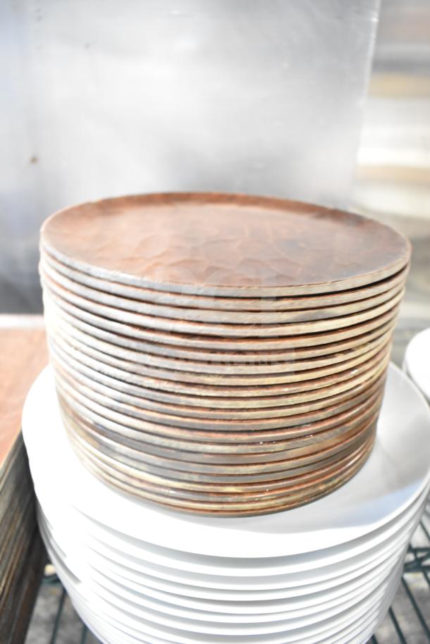 Stacked brown hammered metal plates next to white plates, part of a mixed lot, shown on metal shelving.