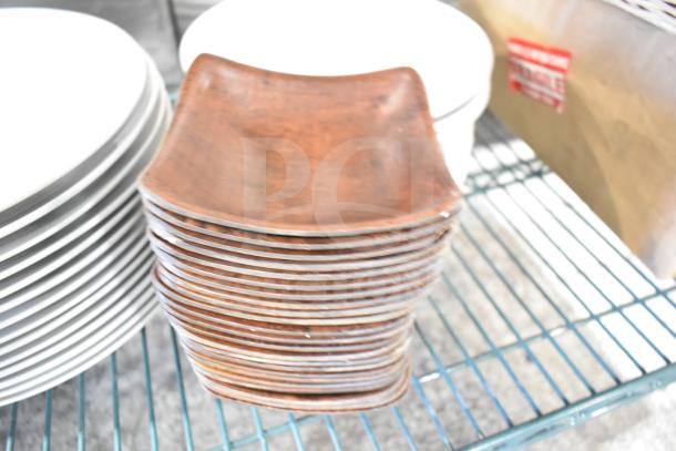 Stack of rectangular wooden plates on a metal rack, showing slight wear, next to white ceramic plates.