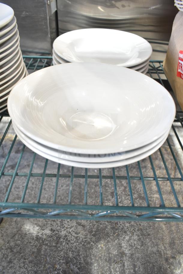 White stacking bowls on a metal shelf, part of a mixed auction lot with plates and baskets, in used condition.