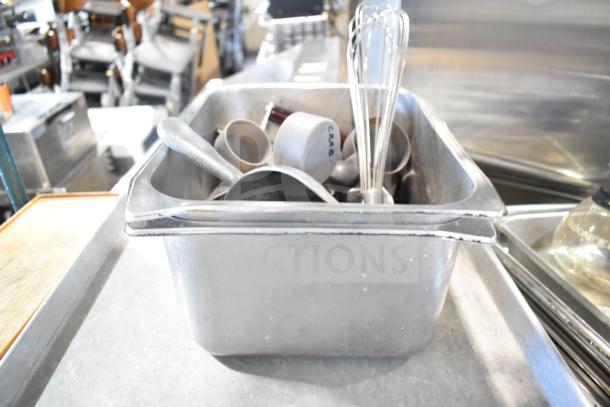 Auction lot including baking pans, stainless steel bins, china cap strainer, stock pot, cutting boards, knives, and utensils.