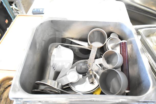 Stainless steel drop-in bin containing assorted measuring cups and spoons, part of a mixed kitchen lot for auction.