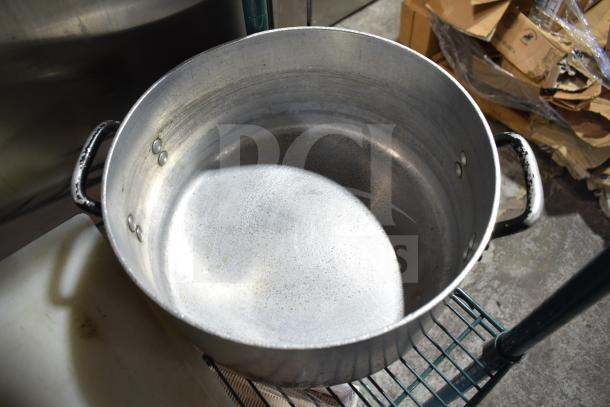 Large metal stock pot with two handles, showing signs of wear. Part of an auction lot including various kitchen items.
