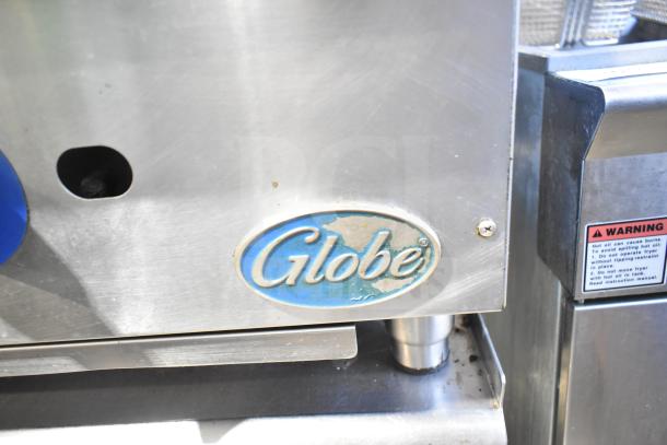 Globe commercial gas charbroiler grill, stainless steel, on stand with casters. Visible logo and warning label.