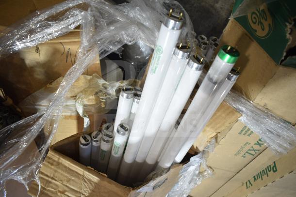 12 new scratch and dent fluorescent tube lights in open box, some wrapped in plastic. Labels show GE branding.