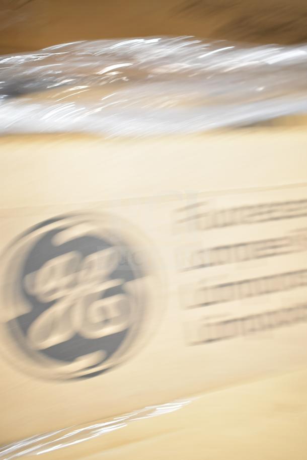 Cardboard packaging with GE logo containing 12 new scratch and dent items, including fluorescent tube lights. Wrapped in plastic.