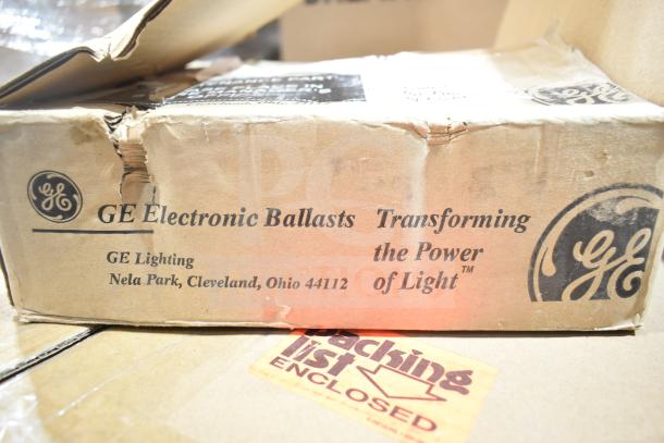 Cardboard box containing GE Electronic Ballasts, displaying brand labels and address, condition shows visible dents and scratches.