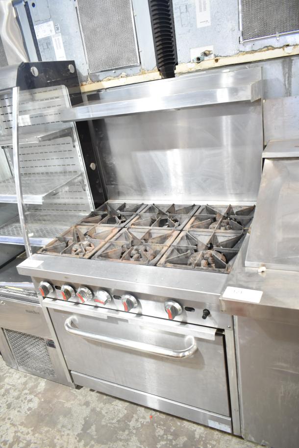 Commercial gas-powered 6 burner range with oven, over shelf, and backsplash in used condition. Stainless steel finish.
