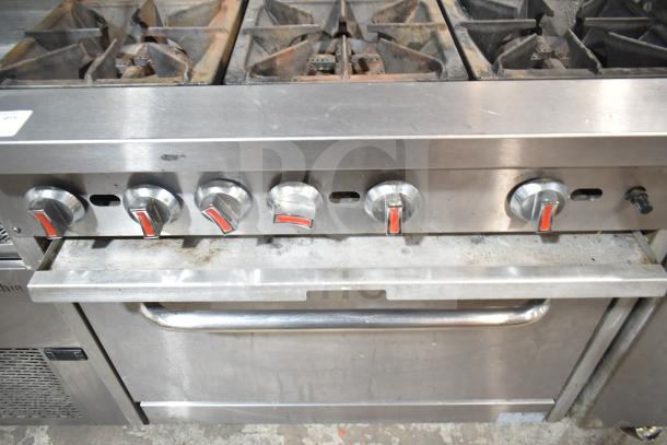 Commercial gas-powered 6 burner range with oven, over-shelf, and backsplash. Stainless steel, visible wear, functional knobs.