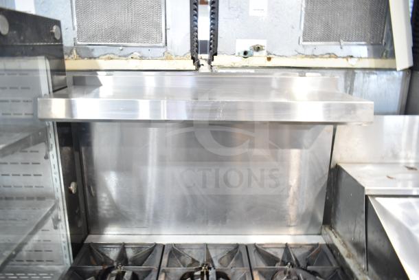Commercial gas-powered 6 burner range with oven, featuring over shelf and back splash. Stainless steel, used condition.
