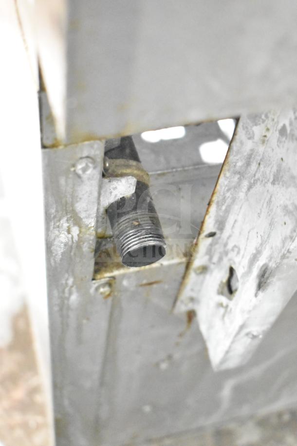 A close-up of the gas connection on a commercial 6-burner range with oven. Metal body shows signs of wear.