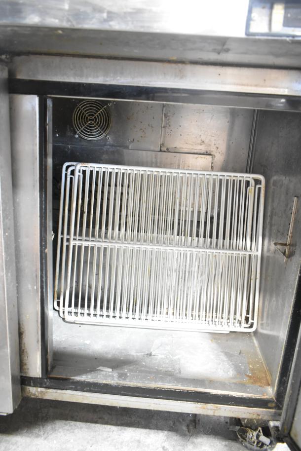 Migali C-SP72-30BT sandwich salad prep table interior. Features wire shelving and commercial casters, showing wear.