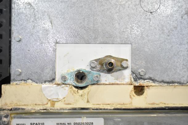 Manitowoc SD0452A ice machine head on SPA310 dispenser, visible wear and corrosion around fittings, model and serial numbers shown.