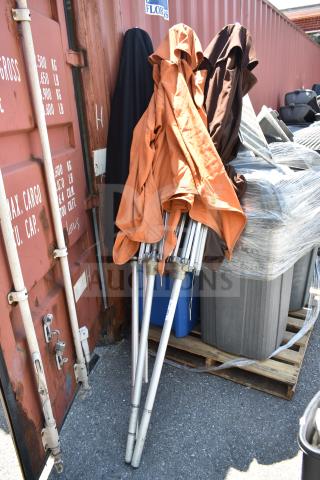Three patio umbrellas, varied colors, folded with metal frames. Used condition, resting against a shipping container.