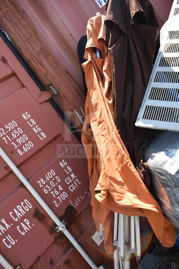 Three patio umbrellas with orange and brown fabric, folded and leaning against a metal container. Visible wear on fabric.