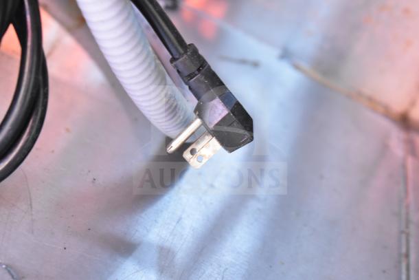 Power cord plug of a commercial workstation with Alto Shaam 200-CW cold pan and steam wells on a metal surface. Plug appears intact.