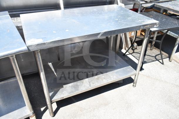 Stainless steel commercial table with under shelf, showing surface wear. Ideal for kitchen use, sturdy design.