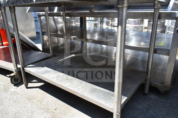 Stainless steel commercial table with under shelf and casters, showing moderate wear, suitable for kitchen use.