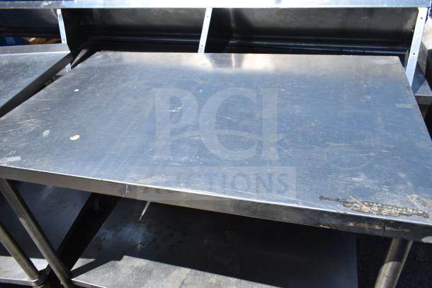 Steel commercial table with undershelf, scuffs on the surface, sturdy metal legs, ideal for kitchen or industrial use.