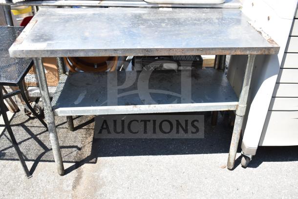 Industrial metal commercial table with under shelf, showing signs of wear and rust. Suitable for heavy-duty use.