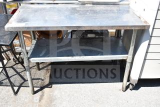 Industrial metal commercial table with under shelf, showing signs of wear and rust. Suitable for heavy-duty use.