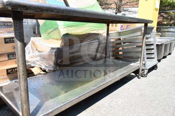 Commercial table with under shelf, metal construction, moderate wear, situated outdoors. Ideal for industrial use.